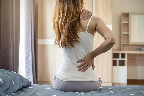 Mulher sentada na cama com dor nas costas